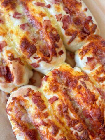 Three baked bread rolls topped with melted cheese and diced ham, placed on a parchment-lined surface.
